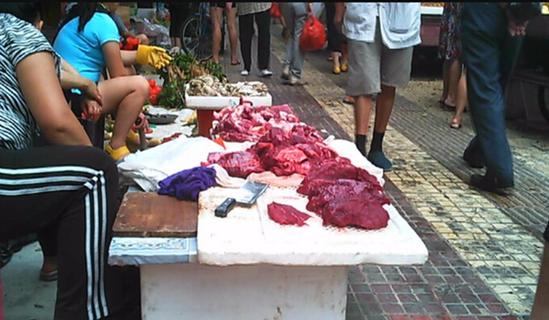 身穿黑白条纹衣服的女子将批发来的老母猪肉，拿到农贸市场外，当作“牛肉”出售。