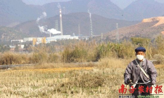 1月15日，仁化县五一村一家冶炼厂正在生产。一位村民戴着口罩从村道经过。 刘龙飞 摄
